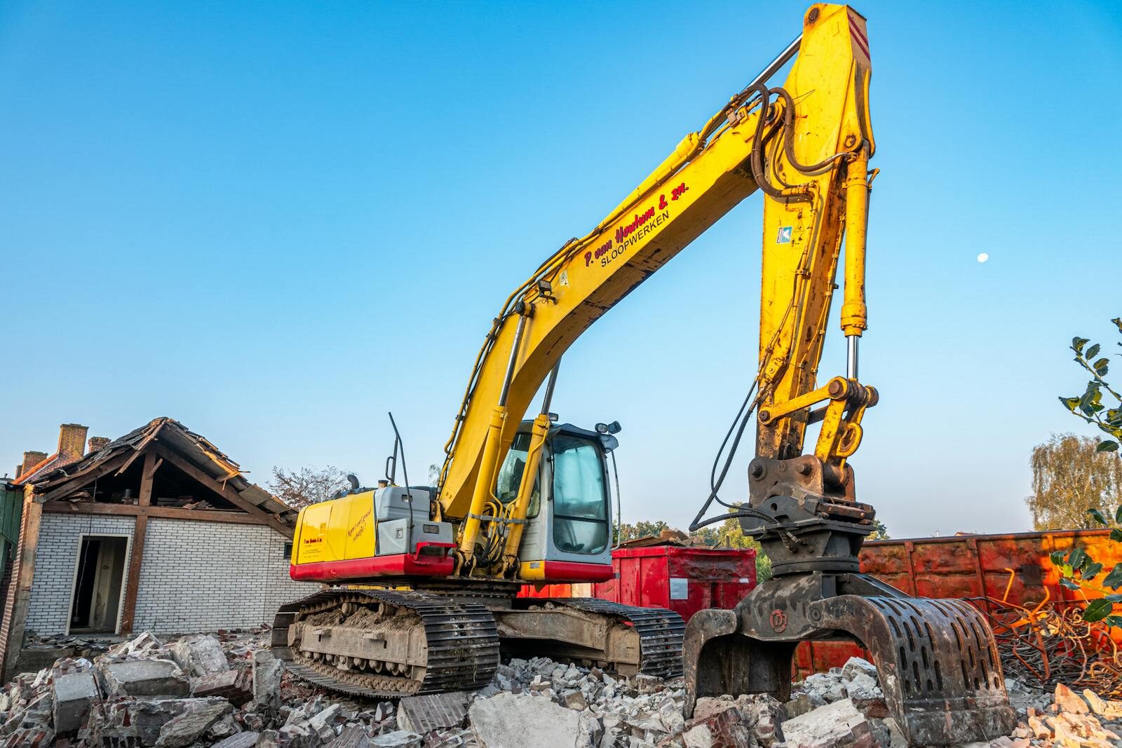 A large Atlas Demolition excavator dismantling a wood-framed residential house in a Charlotte suburb, with workers using water cannons for dust suppression.